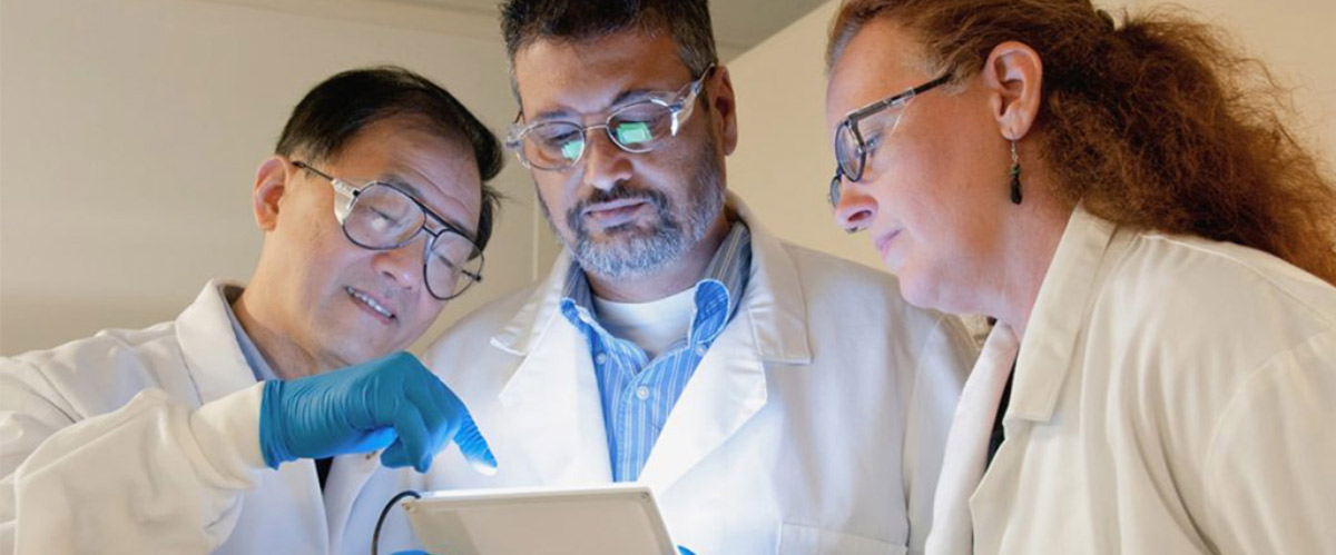 Three researches looking at results on a device, image by the National Cancer Institute.